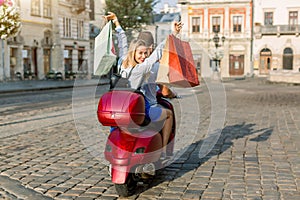 Back view of young couple riding red scooter on a sunny day in old European city. Pretty happy blond woman with shopping