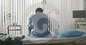 Back view of young desperate man sitting at hospital bed alone