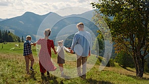 Back view family walking on mountains hill sunny day. Summer vacation together.