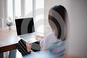 Back view of young female employee in casual wear typing on mockup black screen laptop during working day in home office. Working