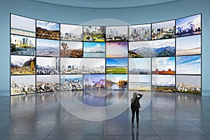 Back view of young female looking at video wall in television production room as technology concept with colorful screens and