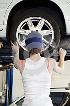 Back view of young female mechanic working on lifted car's tire in automobile repair shop