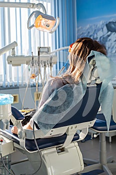 Back view of young female patient visiting dentist office sitting at dental chair. Clinic stomatology