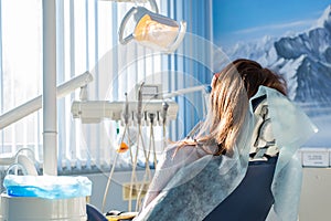 Back view of young female patient visiting dentist office sitting at dental chair. Clinic stomatology