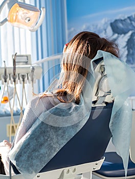 Back view of young female patient visiting dentist office sitting at dental chair. Clinic stomatology