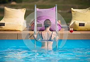 Back view young female in swimsuit coming out from the water of a swimming pool at the resort