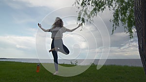 Back view of young fit woman practice yoga on coast near the lake or sea. Woman doing Standing Half Lotus pose