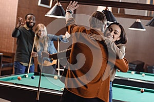 back view of young friends hugging beside pool table