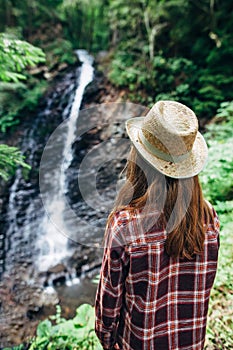 Back view of young girl from afar admires waterfall