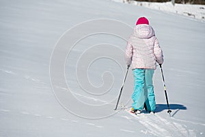 Back view of a young girl crossing a fresh snow with back country skis.