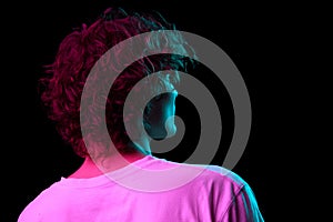 Back view of young hairy man, student in white tee isolated on dark background in neon light. Concept of emotions