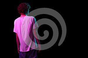 Back view of young hairy man, student in white tee isolated on dark background in neon light. Concept of emotions