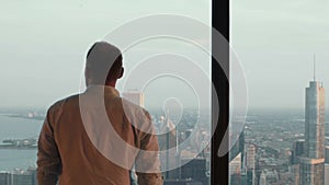 Back view of young handsome man standing near a window in skyscraper and looking on panorama of Chicago, USA.