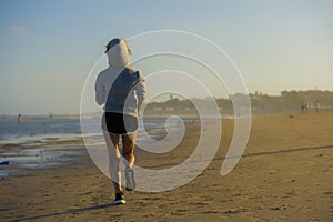Back view of young happy and attractive fit woman in hoddie running on the beach in outdoors jogging workout in fitness training a