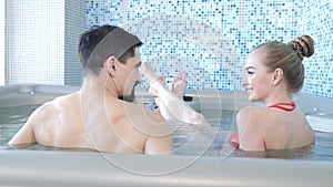 Back view of young loving couple relaxing in spa resort pool. Honeymoon couple enjoying together in swimming pool in