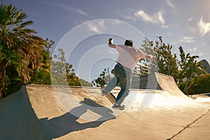 Back view of young man doing tricks on his skateboard at the skate park. Active sport concept