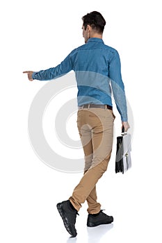 Back view of young man holding suitcase and pointing finger