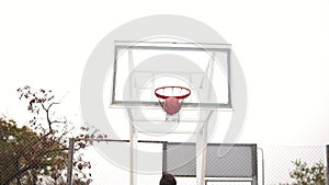 Back view of young man playing basketball and throwing a ball to the basket successfully. Slowmotion shot