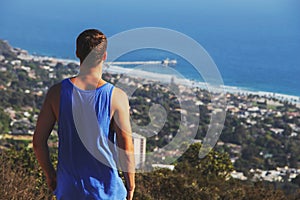 Back view of young man in a tank shirt looking at sea landscape from a mountain top