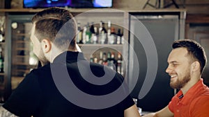 Back view of young man with tattoed hands dressed in black t-shirt walking through the cafe to his friends. Two women