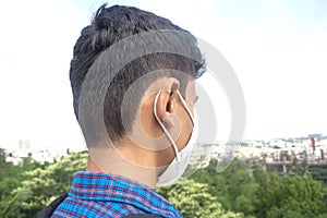 Back view of young man wearing face mask. city background.