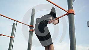 Back view of young muscular man doing Muscle Up exercise on bar outdoors