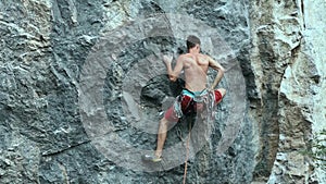 Back view young muscular man rock climber climbing on tough sport route outdoors on a vertical cliff