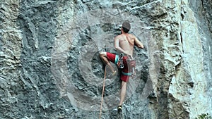 Back view young muscular man rock climber climbing on tough sport route outdoors on a vertical cliff