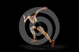 Back view of young muscular woman running isolated on black background. Sport, track-and-field athletics, competition