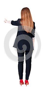 Back view of young redhead business woman pointing at wall.