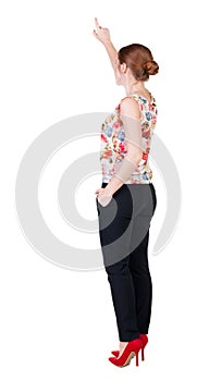 Back view of young redhead business woman pointing at wall.