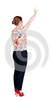 Back view of young redhead business woman pointing at wall.