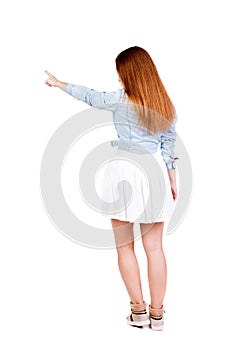 Back view of young redhead woman pointing at wall. beautiful gir