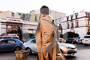 Back view of young stylish man in trench coat walking through street