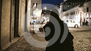 Back view of young stylish woman walking through the deserted lane late at night to main street, urban road.