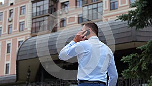 Back view of young successful male walking in street in town and calling on smartphone. Rear of one male outdoors