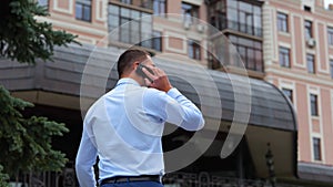 Back view of young successful male walking in street in town and calling on smartphone. Rear of one male outdoors