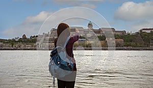 Back view young tourist woman take a picture by Photo camera of a smartphone with blue sky scene in the city at Buda Castle Royal