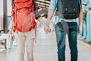 Back view of young traveler couple with backpack holding hand at train station