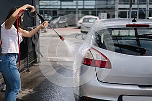 Back view of young woman cleaning her car on self service car. Female washing with jet sprayer. White foam on car