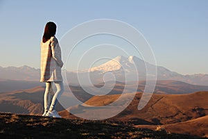 Back view of young woman in a coat admiring the view of Mount Elbrus