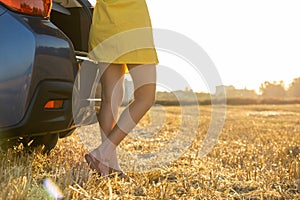 Back view of young woman driver legs in yellow summer dress standing near her car