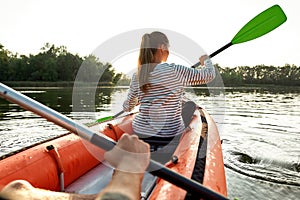 Back view of young woman enjoying kayaking with her boyfriend in a river on a summer day