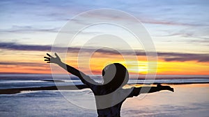 Back view of young woman feeling happy and freedom as silhouette with raised arms against calm sunset beach background