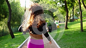 Back view of a young woman in fuxy leggins running in the sunny city park exercising outdoors. Steadicam stabilized shot