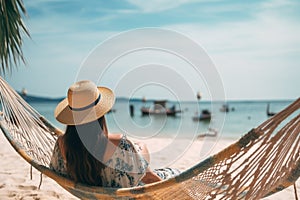 Back view of a young woman in a hammock on a tropical sandy beach during the sunset