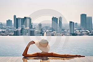 Back view of young woman in hat relaxing in swimming pool on the roof top of hotel and enjoy cityscape