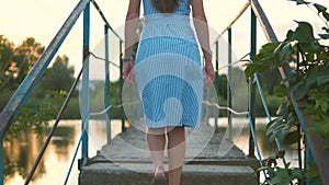 Back view of young woman with long hair walking up the stairs outdoors in summer park at sunset.