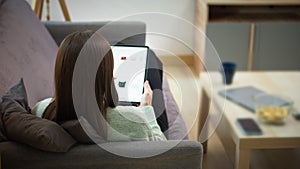 Back view young woman lying on couch and using digital tablet for shopping online