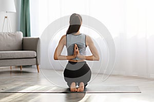 Back view of young woman practicing yoga at home